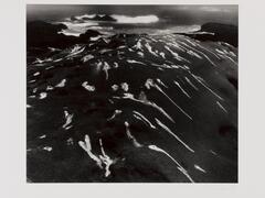 Photograph of long white streaks on a hilly seaside landscape.