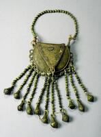 Round brass purse with loops around the outer edge. Attached to each loop is a string of brass beads and a crotal bell. The handle is composed of brass beads. The edge of the flap closure is decorated with concentric semi-circles. 