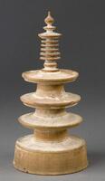 Wooden miniture model of a tower, comprised of a round base, a bar in the middle where three larger discs and six or seven small discs are inserted. A bulb-shaped ornament rests on top.