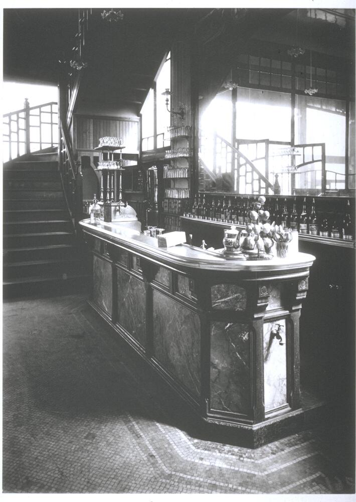 Photograph of the interior of a bar with a mirror and staircase behind.