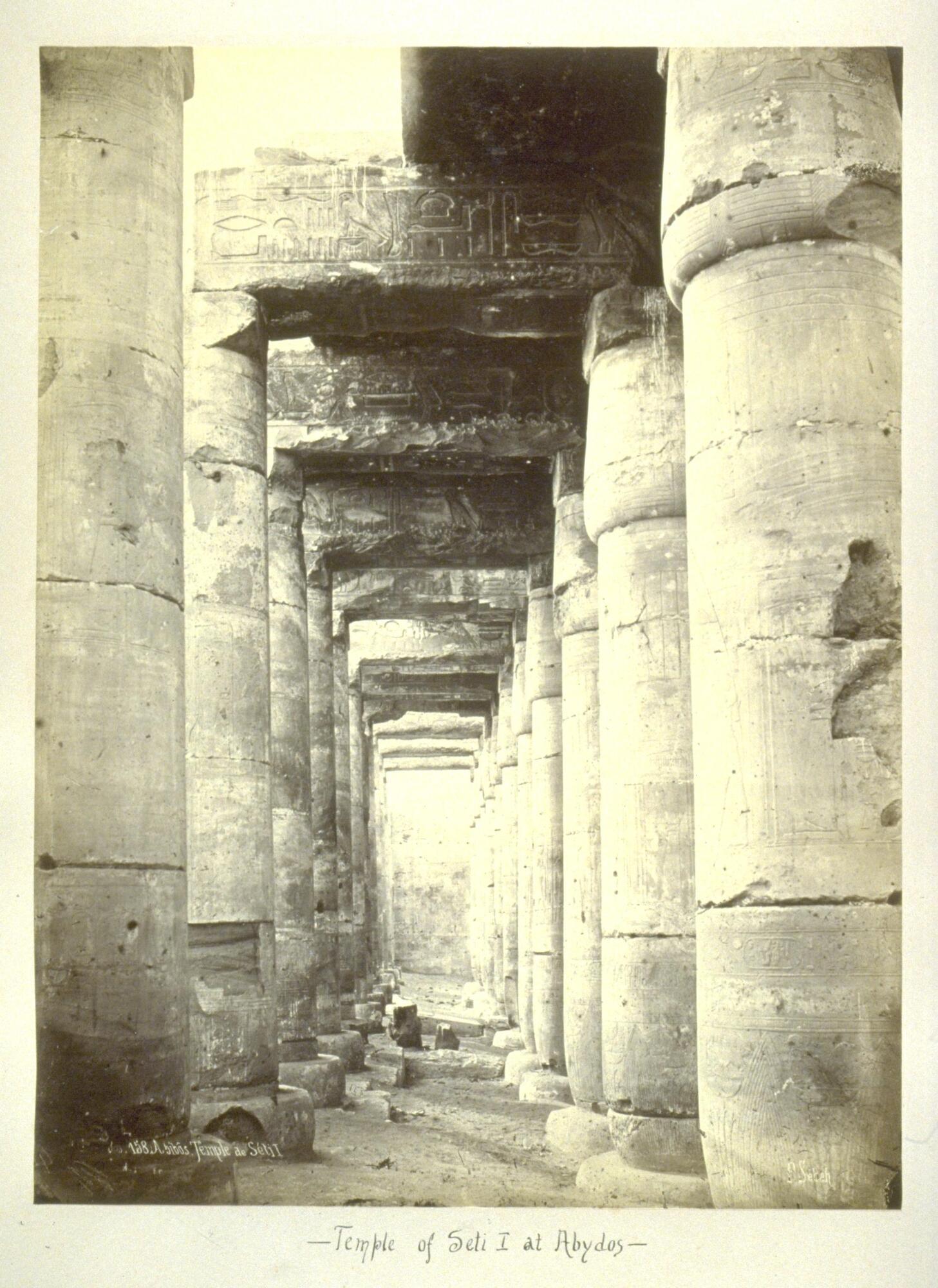 This photograph shows a narrow corridor flanked on either side by two rows of massive, stone columns. 