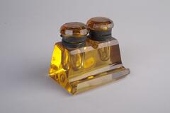 An amber, two-bottle inkwell.  Rectangular in shape with a lip that acts as a pen rest.