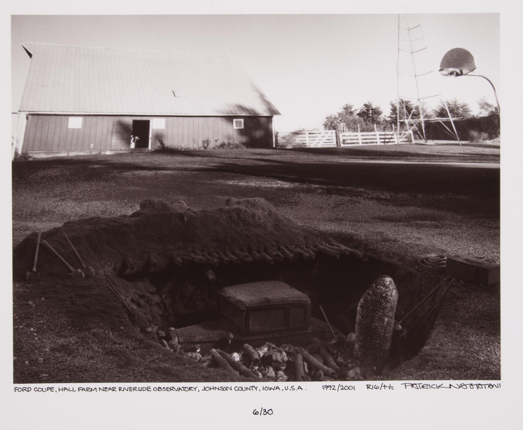 Car under excavation at a farm with a barn in background.