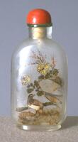 A glass snuff bottle with bids and flowers painted on the surface of it. On the top is a coral stopper in a green glass collar.