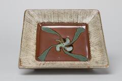 Square plate with textured mishima-style border. The interior of the plate is brown with a trailed green design.