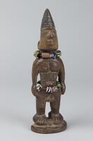 Standing male figure on a round base, part of which has broken off. The hands are at the sides and there are geometric designs on the abdomen. Around the waist and neck are strings of multi-colored beads. The hair is in a rounded comb-like shape with horizontal grooves. 