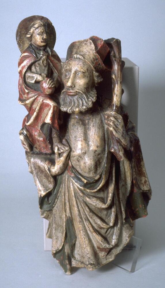 A standing, bearded figure of St. Christopher, broken off at the knees, holds the Christ child on his right shoulder while leaning upon a staff in his left hand. The child, whose head is encircled by a halo, wears a long cloak over his robe and rests his left hand upon an orb in his lap. The red and brown polychromy is a later addition.