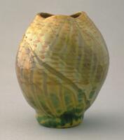 This oval-shaped vase has an irregularly shaped mouth. The decoration, which consists of numerous layers of glass, has green and brown glass in the bottom third; a swriling brown and cream glass the overlays from the foot up to the lip of the vessel, and finally a horizontal pattern of warm brown dots (which are pulled into bands around the widest part of the vessel) that begins at the top.