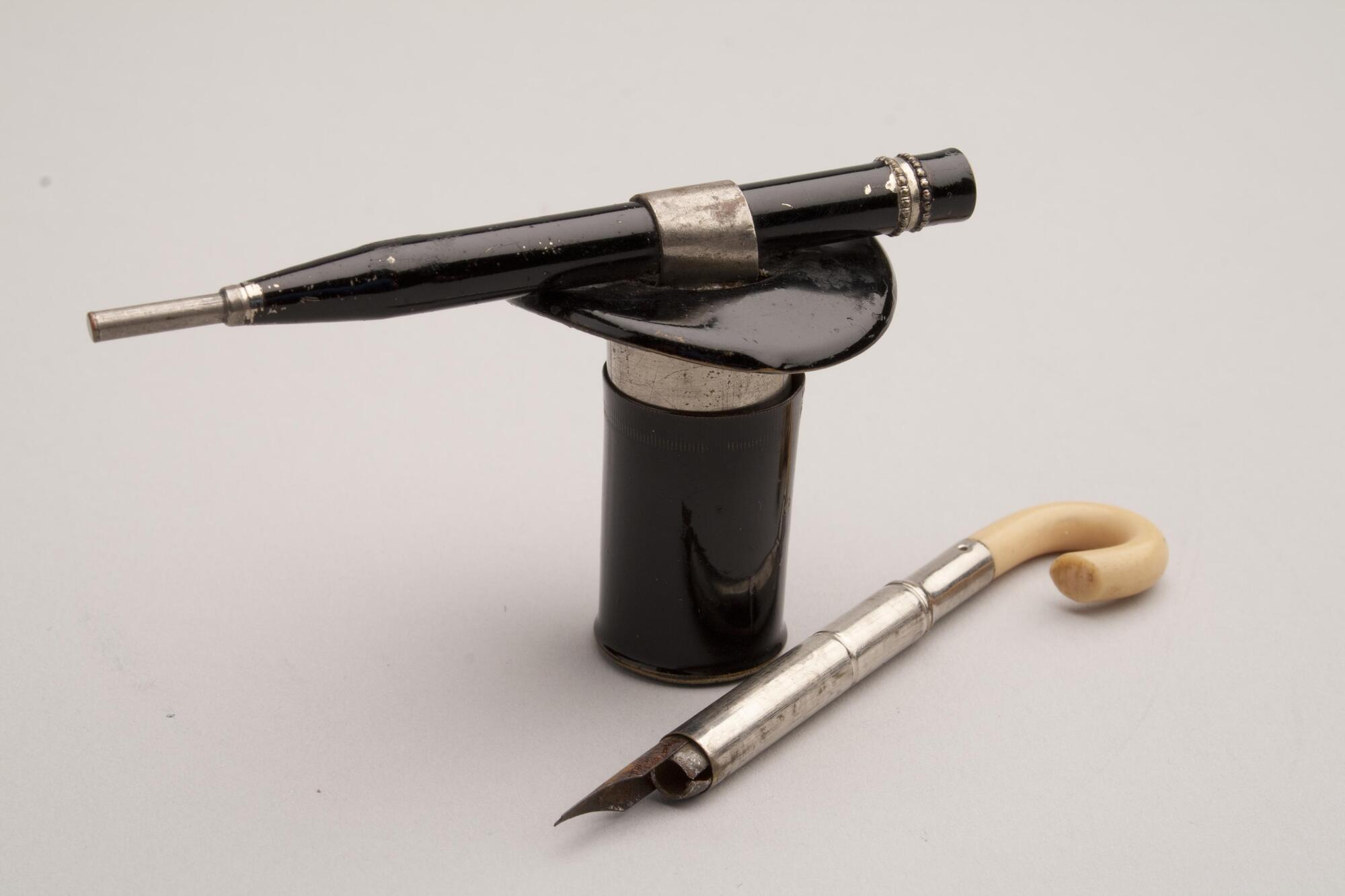 A metal inkwell in the shape of a black tophat.  A pen shaped like a cane is included. The handle of the cane is ivory.