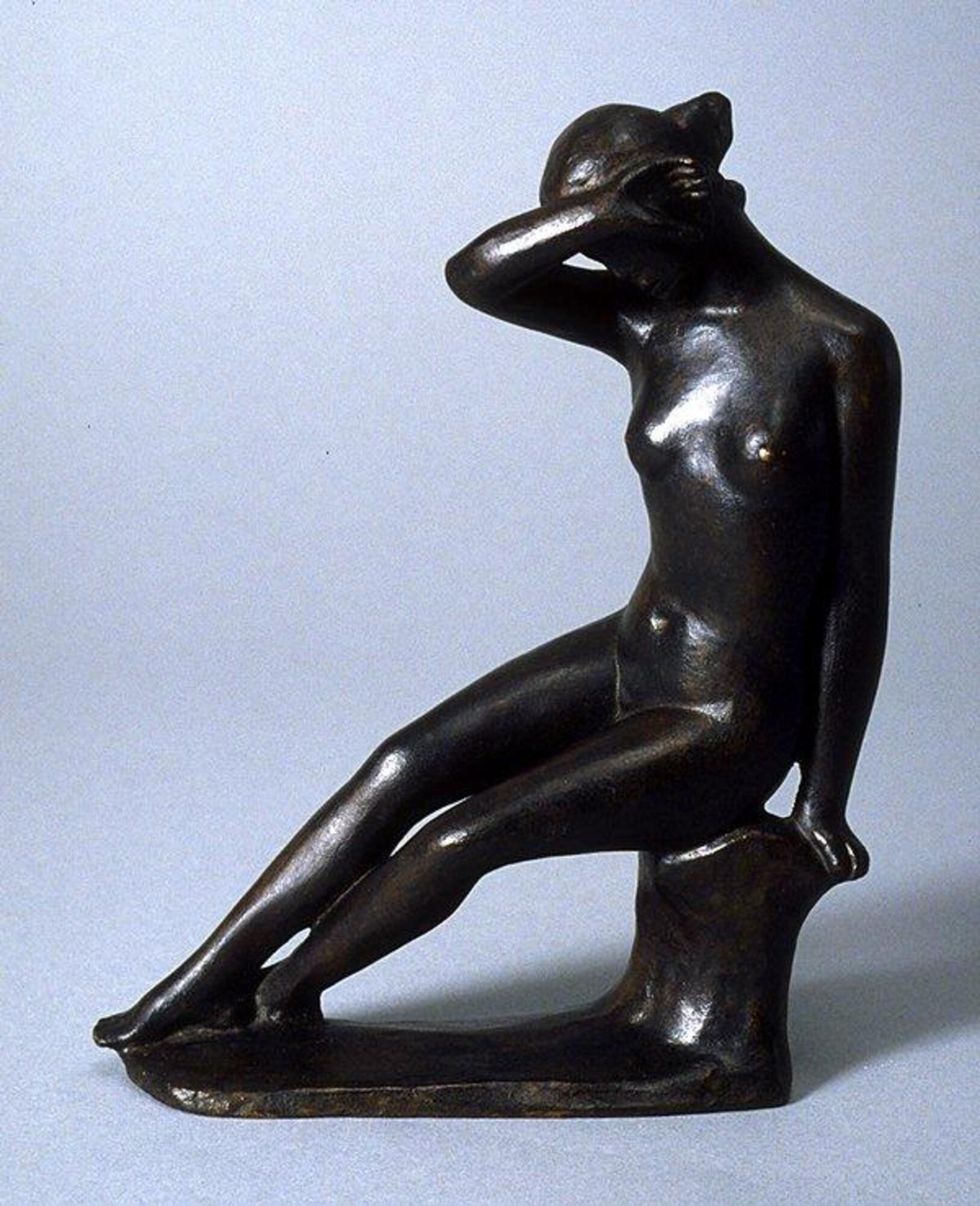 This is a 21cm tall bronze sculpture of a nude female figure seated on a stump-like form with her legs extending out in front of her and crossed at the ankles. She leans the weight of her body on her left arm, as her left hand grasps the edge of the stump. Her right arm is bent and raised, with the back of her hand resting against the left side of her head.  She is gazing downward and her arm seems to be shielding her face. Her hair is pulled back and gathered in a knot. The patina is dark brown and the metal surface has a uneven appearance.
