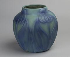 A light green vase with a blue flower decoration carved onto the sides.