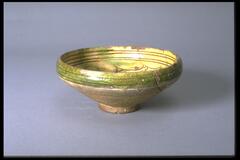 Baked clay bowl. Interior is symmetrical incised designs of two pairs of animals cut through glossy, fine-crackle top glaze and cream slip, showing brown and some green patches. The exterior has drops of glaze on upper part run down. Paste is light brown, medium fine and medium hard. Interior tripod marks indicate possible double firing. The colors are green and cream on the interior. On the exterior the upper part is green over cream slip and the lower part is gray-brow. The rim is entirely green. The bowl is mended and slightly restored. 