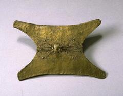 Flat, rectangular piece of brass with concave sides and a central raised knob. Along the center is a design consisting of a braided pattern, concentric semi-circles, and small, raised dots. 