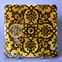 This polychrome and glazed square tile is decorated with a symmetrical design of flowers and leaf arabesques in deep aubergine and yellow. It is covered in a lustrous glaze with black underglaze. The tile matches the style and decorative features of other 16th century Turkish tiles. 