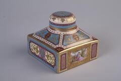 Inkwell made of porcelain has a square shape body and a round lid cover. It is decorated in detail patterns of blue, gold and white; and it has scenes of thr royals on the side body of the inkwell.