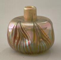 This small bottle consists of orange and green iridescent glass with a brown pointed leaf or blade design. The bottle has been pinched in at the sides.