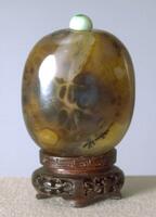 A round agate pebble snuff bottle. On top os the snuff bottle is a jadeite stopper.&nbsp;
