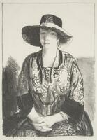 Seated woman in a floppy hat. Her hands are folded in her lap.
