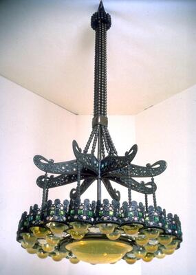 Chandelier consists of a bronze post with eight arms (inset with colored glass) from which hangs two rings of yellow translucent glass half-dome glass surrounding a single, large yellow glass half-dome globe in the center.