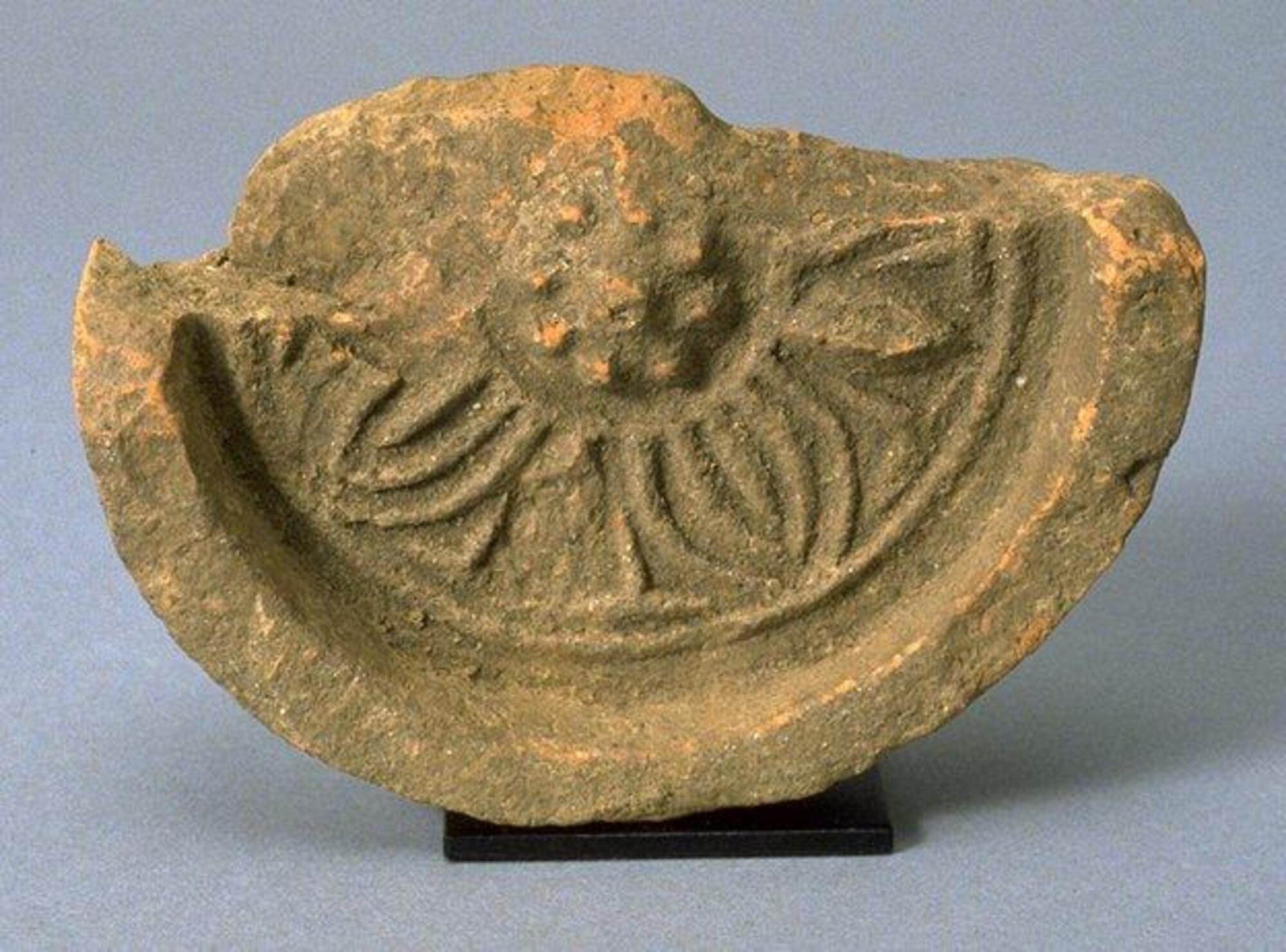 A fragment of unglazed earthenware: approximately half of a round, molded roof tile, depicting a central lotus flower in relief. 