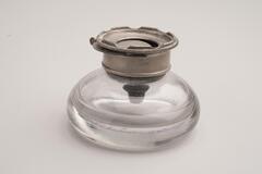 A round inkwell with a pewter lid. The lid has a grooved edge encircling it.