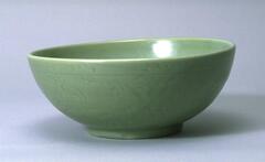 This is a round stoneware bowl on a footring with a direct rim. The exterior is incised with a floral meander and covered in a green celadon glaze. 