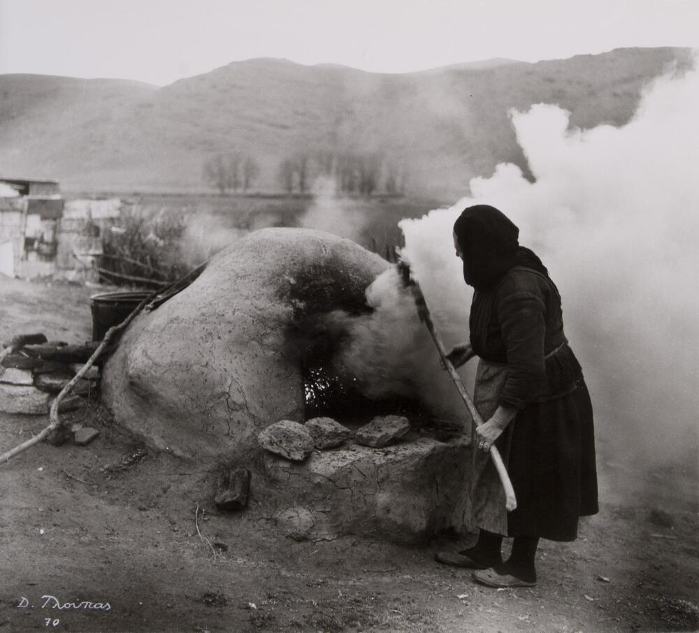 A woman at an outdoor rock stove. In the background, there are hills and vast landscape.