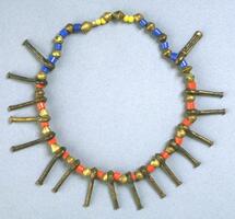 Belt with blue, yellow, orange and brass beads. There are pendants in the shape of nail heads and one pendant with a woven pattern. 