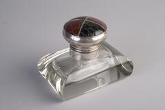 A rectangular glass inkwell with rounded edges.  The lid is metal with brown and black leather.