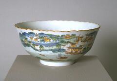 A bowl with a landscape scene that has buildings, a river, and trees. It is on a footing and a wavy rim.