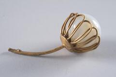 <br />
A clouded glass orb in a brass-colored metallic cap comprised of looped petal-like shapes connected to a thin metal stem.