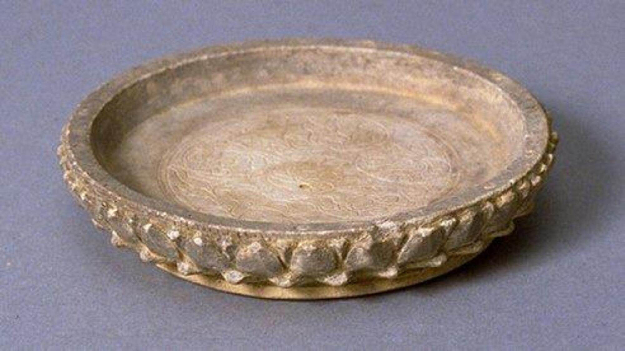A nearly flat, large, shallow stoneware dish, the interior with a delicately incised floral scroll pattern, and the upturmed rim adorned with robustly modelled lotus petals, all on a broad and secure foot.