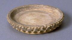 A nearly flat, large, shallow stoneware dish, the interior with a delicately incised floral scroll pattern, and the upturmed rim adorned with robustly modelled lotus petals, all on a broad and secure foot.