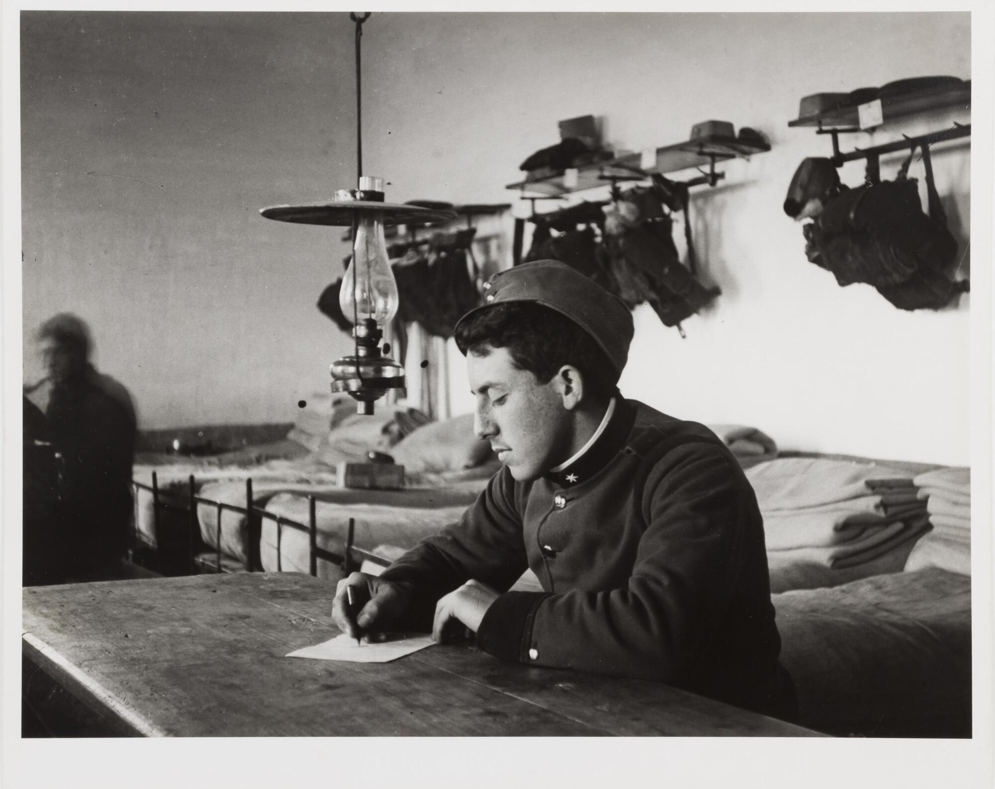 Photograph of a soldier sitting at a desk and writing on a piece of paper.