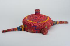 Hat composed of primarily red beads, with yellow, green, and blue beaded designs and two longer protuberances and three smaller ones.