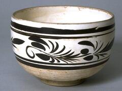 A deep stoneware bowl with direct rim on a footring, covered in a white slip, with painted underglaze black calligraphic floral meander and bands around the body.