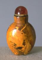 A root amber snuff bottle with a coral bead stopper in a green tinted ivory collar.
