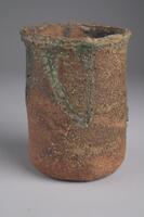 Rough ceramic cup with a cylinder body. Red/brown color with strips of green/grey near the top