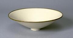 This very thin porcellaneous stoneware, wide flaring, conical bowl with direct rim is on a straight foot ring. The interior is incised with a pomegranate design and covered in a creamy white glaze. The unglazed rim is finished in a mounted silver band.  