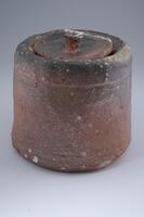 This cylindircal jar has a circular lid with a small handle. The natural ash glaze creates a mix of green, black, gray, and reddish hues.