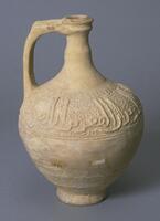 <br />
The unglazed jug has a bulbous body with a narrow neck which is half the height of the body. A slight bulging occurs midway up the neck. A handle is joined to the neck below the lip and extends to the shoulder of the body. <br /><br />
A <em>Naskhi</em> Arabic inscription, worked in barbotine technique against a background of unordered small bosses and open circles, runs around the upper part of the body. <br />
 