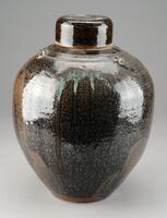 Large jar with lid and mottled brown and black glaze.  An incised wavy line circles the upper portion of the body.