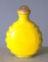 A yellow circular glass snuff bottle with ridges on the sides. On the top is an agate stopper in a horn collar.
