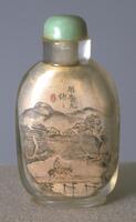 A glass oval shaped snuff bottle with a landscape scene; there&#39;re mountains, houses, a river, and a man riding a horse over a bridge. On the top is a jade stopper.