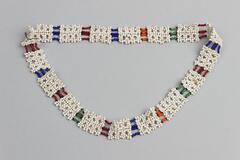 Beaded necklace with white beads, open weave squares attached together by four rows of beads in red, orange, blue and green. White tag attached.