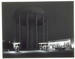 Photograph of a gas station with a water tower in the background.