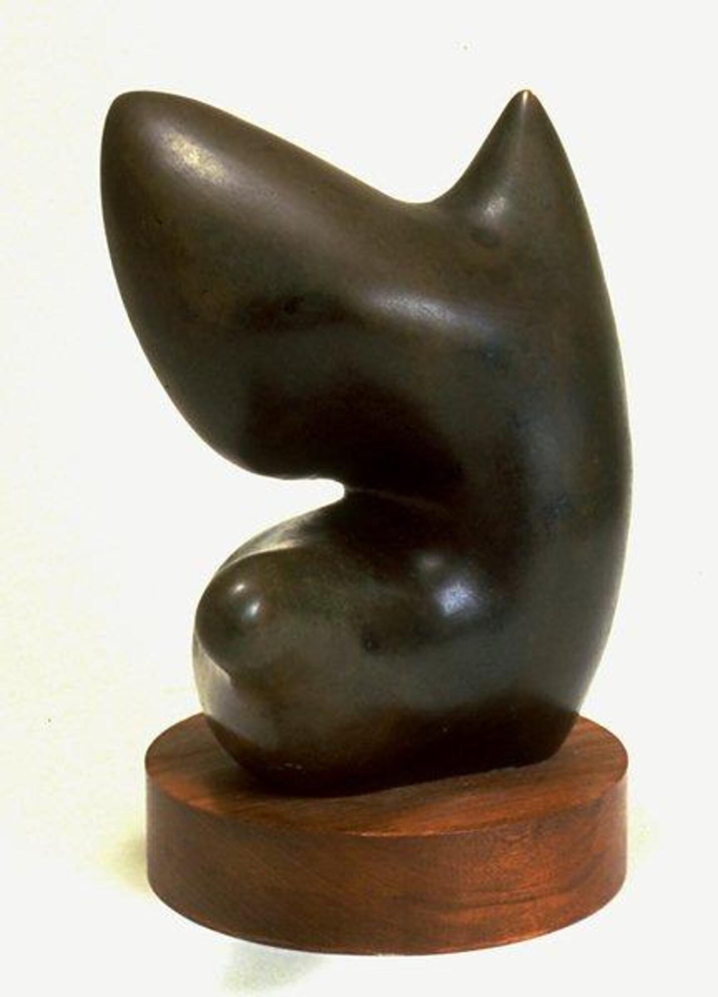 A biomorphically abstract sculpture of bronze. Bulbous at the bottom, the shape stretches and narrows in the middle and then expands into a larger shape from which two rounded points rise.