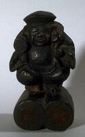 This woodwork depicts Daikoku, the god of good fortune, who is associated with farmers. Here he is sitting astride two large barrels of rice, while carrying over his shoulder a large sack, brimming with treasure.  In his right hand he holds a magic mallet, said to be able to produce anything the heart desires when struck.<br />