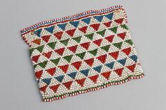 Beaded pouch with one side longer than ther other so it forms a flap over the top. White background wiht red, blue and green triangle design. Trimmed in alternating red and white beads.