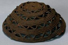 A dome-shaped cap with alternating patterns of straight and wavy linear designs. Between the wavy linear designs are spaces allowing one to see through the cap. 